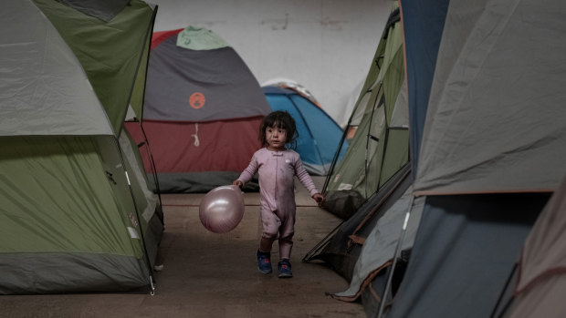 A girl holds a balloon as she walks among tents inside an empty warehouse used as a shelter set up for migrants in downtown Tijuana, Mexico. 