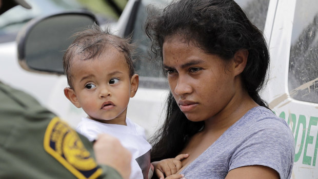 A mother migrating from Honduras holds her 1-year-old child as she surrenders to US Border Patrol agents after illegally crossing the border.