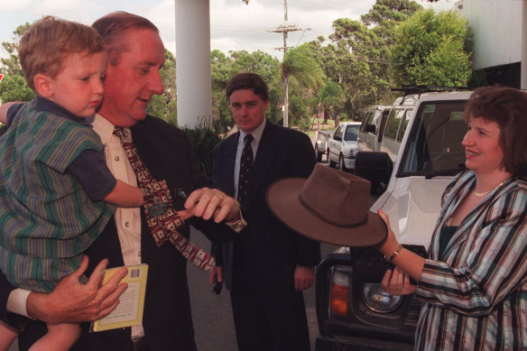 Tim Fischer holding his then two-year-old son Harrison, while being handed his famous hat by wife Judy at a National Party Election Campaign launch party in South Tweed Heads.