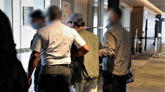 Binjun Xie is escorted to a plane after being arrested.