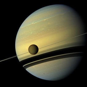 Titan, Saturn's largest moon appears before the planet as it undergoes seasonal changes in this natural-colour view from NASA's Cassini spacecraft.