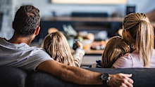 Back view of a relaxed family watching TV on sofa in the living room. man with wife man with children