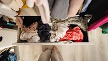 A messy open dresser drawer filled with disorganised clothes in a home closet.