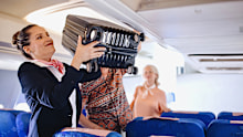 Cabin Crew helps passenger with putting bags and suitcases in overhead locker