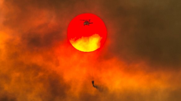 A firefighting helicopter makes a water drop as the sun sets over a ridge burning near Redding, California.