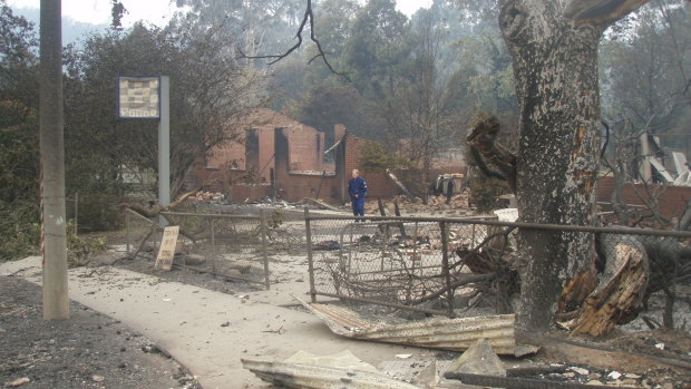 A police officer stands inside what remains of the Marysville station days after the fire. The Total Fire Ban sign can be seen against the fence on the left.