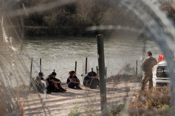 Migrants wait to be processed by Border Patrol along the banks of the Rio Grande River in Eagle Pass last week.