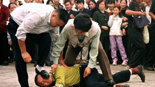 Police detain a Falun Gong protester in Tiananmen Square as a crowd watches in Beijing.