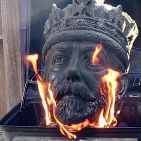 The head of a statue of George V is burnt on a barbecue