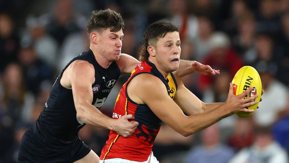 Jake Soligo of the Crows handballs whilst being tackled by Sam Walsh of the Blues.