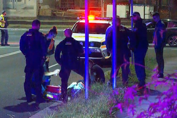 An injured police officer sits in the gutter after he was injured by a man believed to be driving a stolen car.