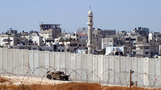 An Israeli army vehicle patrols along Israel’s separation barrier at the Qalandiya refugee camp, background, in the outskirts of the West Bank city of Ramallah Saturday, July 10, 2004. While Israeli enlisted American help, the Palestinians sought Europe’s backing Saturday for U.N. enforcement of the nonbinding international court ruling that found Israel’s massive West Bank barrier to be illegal. (AP Photo/Nasser Shiyoukhi) 