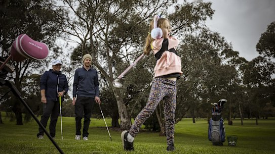 Matilda Gray is watched by her  father Lincoln and PGA  Community Instructor Claire Trail at the Northcote Public Golf Course. Photograph by Chris Hopkins