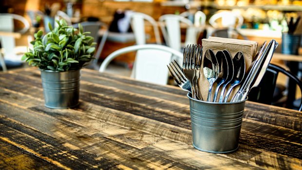 A warm cafe interior with wooden table, cutlery, pot plant and food counter in the background Generic cafe restaurant
iStock