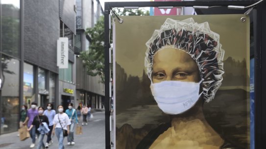 People wearing face masks to help protect against the spread of the new coronavirus walk by an advertisement of a hair shop at a shopping district in Seoul, South Korea, Tuesday, May 26, 2020. (AP Photo/Ahn Young-joon)