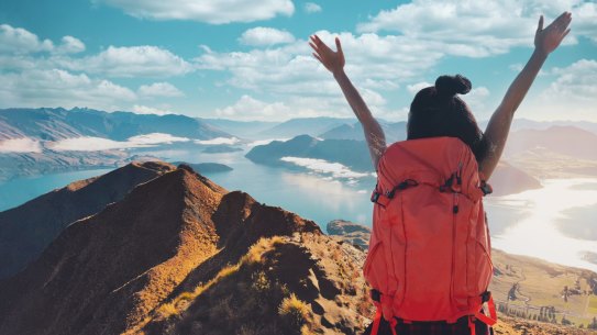 Young asian women hikers climbing up on the peak of mountain near ocean. Woman hiking in the mountains standing on a rocky summit ridge with backpack. Roys peak track, South island, New Zealand. roy's peak nz