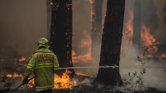 Firefighter Adam Brown from Fire & Rescue NSW protects properties near South Taree from an out of control bushfire on Sunday.
