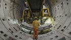 Workers labour beneath a tunnel-boring machine at a construction site.