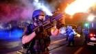 A member of the St. Louis County Police tactical team fires tear gas into a crowd of protesters. 