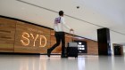 Sydney Airport departures sign and passenger wheeling luggage