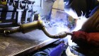 An employee welds parts on to a automobile catalytic converter emission control device.