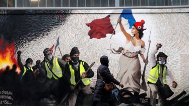 A woman passes by a mural by street artist PBOY depicting Yellow Vest (gilets jaunes) protesters inspired by a painting by Eugene Delacroix, "La Liberte guidant le Peuple"  in Paris on Thursday.