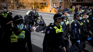 A man is taken to the ground by police as a flare goes off in the background at Melbourneâ€™s anti-lockdown rally.