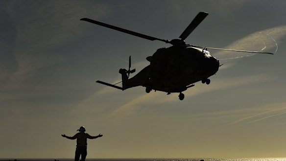 An Aviation support crew member signals during take off of a MRH90 or Taipan helicopter from 808 Squadron attatched to the HMAS Canberra in 2015.