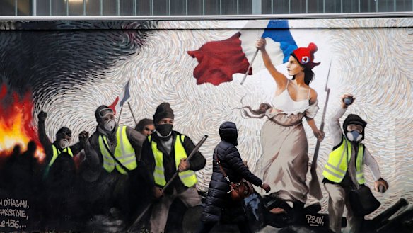 A woman passes by a mural by street artist PBOY depicting Yellow Vest (gilets jaunes) protesters inspired by a painting by Eugene Delacroix, "La Liberte guidant le Peuple"  in Paris on Thursday.