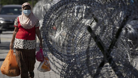 A woman walks home with groceries next to barbed wire in the locked-down area of Selayang Baru in Kuala Lumpur, Malaysia.