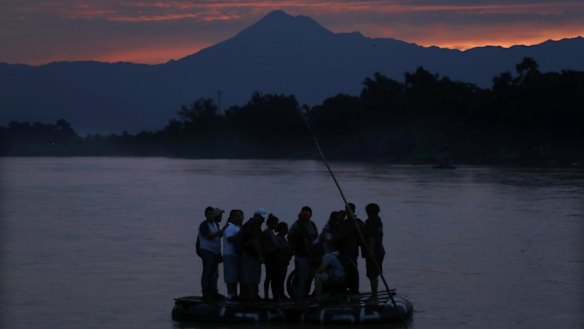 Central American migrants stand on a raft to cross the Suchiate River from Guatemala to Mexico, with the Tacana volcano in the background, near Ciudad Hidalgo, Mexico.