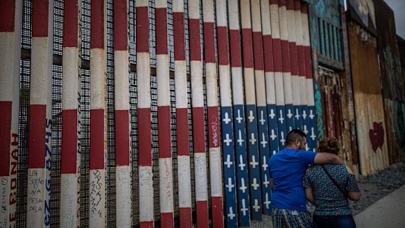Pedestrians pass in front of a section of a US-Mexico border wall in Tijuana.
