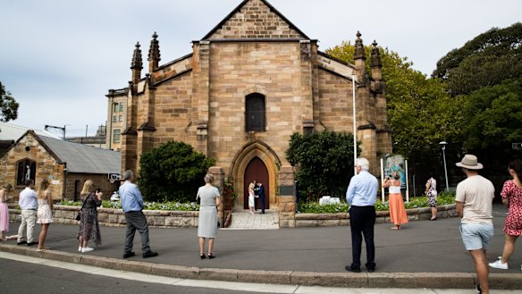 Bystanders, who were not invited to the wedding, practice social distancing on the street while Brigette Leech and Matthew Selby are married by Minister Justin Moffatt, at the Garrison Church in Sydney.