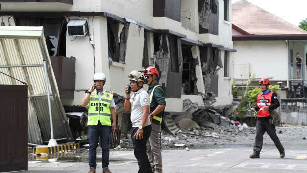 Rescue workers stand near an apartment block that partially collapsed after the strong earthquake in Davao City on Thursday.