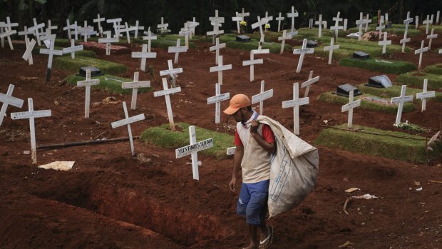 A man looks for discarded plastic near newly dug graves for those suspected of dying from COVID-19 in Jakarta, Indonesia. 