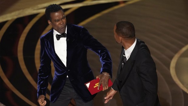 Chris Rock, left, reacts after being hit on stage by Will Smith while presenting the award for best documentary feature.