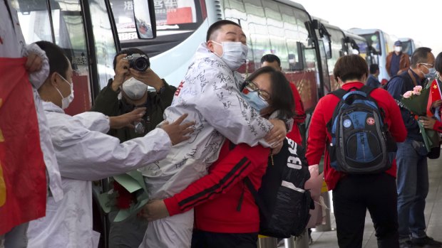 A medical worker, in red, embraces a colleague as she prepares to leave Wuhan after restrictions were lifted.