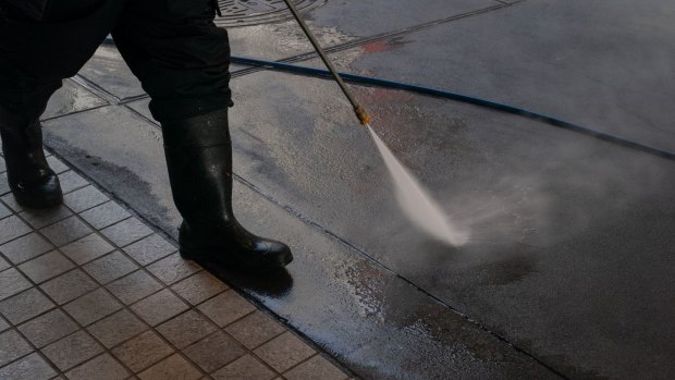 A city cleaner pressure-washes a sidewalk in San Francisco.