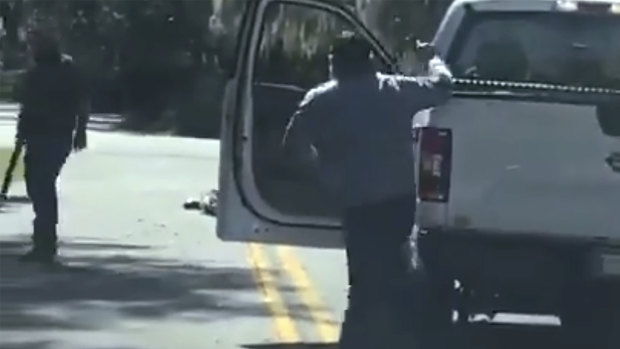 The video purports to show Ahmaud Arbery lying on the road after being shot as Travis McMichael, left, holding a shotgun, and his father, Gregory McMichael, holding a handgun, approach him in Brunswick, Georgia. 