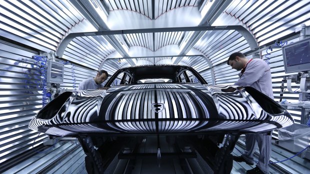 Workers perform quality checks on a Macan sports utility vehicle (SUV) in the light tunnel at the paint shop inside the Porsche Leipzig GmbH factory in Leipzig, Germany.