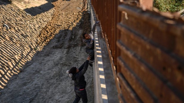 Nelly, a Mexican migrant from Oaxaca, helps her son as they jump the border fence to get into the US to apply for asylum.