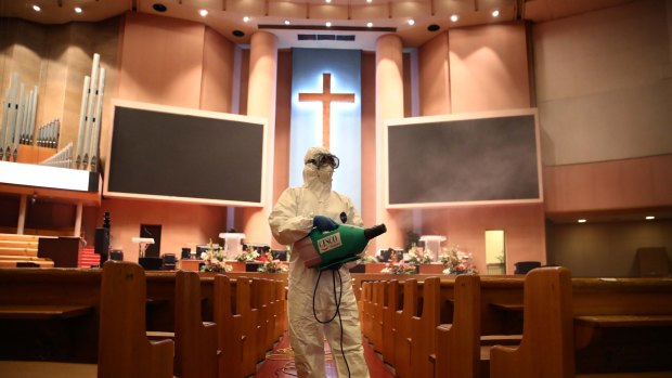 A disinfection worker wearing protective clothing sprays antiseptic solution in a South Korean church.