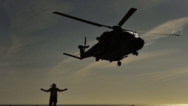 An Aviation support crew member signals during take off of a MRH90 or Taipan helicopter from 808 Squadron attatched to the HMAS Canberra in 2015.