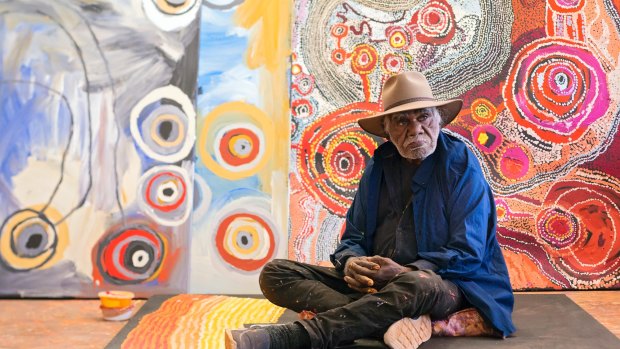 Ray Ken in front of works by Barbara Mbitjana Moore, Tjungkara Ken and Yaritji Young at Tjala Arts in Amata, South Australia.