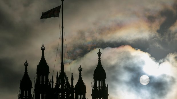 The sun breaks through clouds behind the Houses of Parliament in London.
