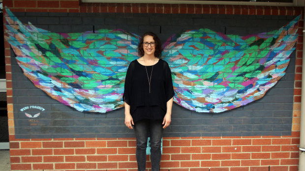 Miriam Fee, standing before her winged artwork, teaches visual art at a Melbourne secondary school. 