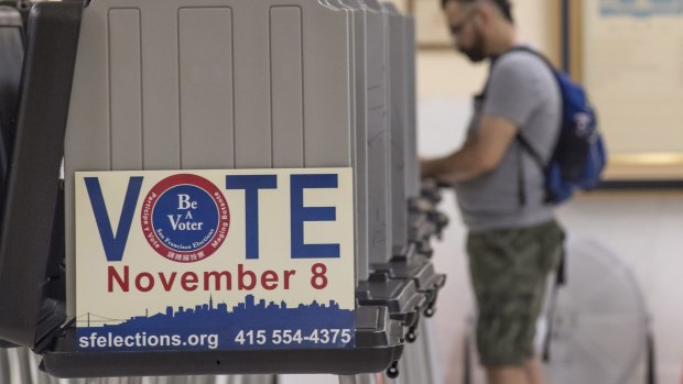 A sign reading "Vote" is displayed on the side of a booth as a voter casts a ballot at the San Francisco City Hall polling location.