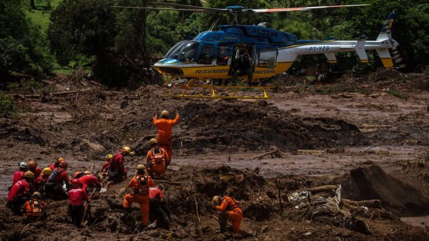 Rescue workers co-ordinate with a helicopter while attempting to remove a body from the debris of a bus after the dam burst in Brazil.