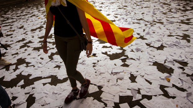 A Catalan independence supporter walks a long a street covered with referendum ballots during a rally in front of the then Spanish Partido Popular ruling party headquarters in Barcelona, Spain, in 2017.