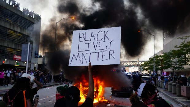 A man holds a Black Lives Matter sign as a police car burns during a protest on May 29 in Atlanta, Georgia. Demonstrations are being held across the US after George Floyd died in police custody on May 25 in Minneapolis, Minnesota. 